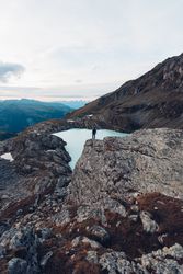 Man standing on rock formation on waterside of frozen lake in the mountain