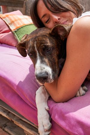 Happy young woman embracing dog while lying on mattress outside