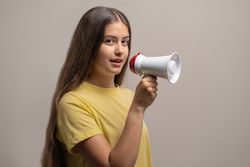 A young woman making an announcement with a megaphone on a studio background.