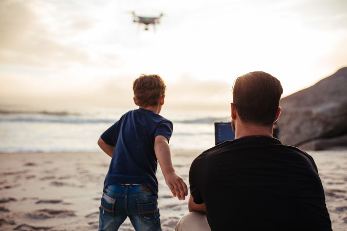 Young man with little boy enjoying flying a drone