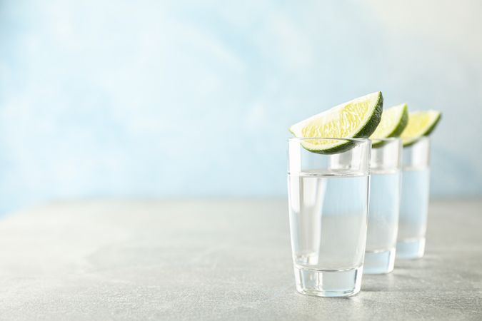 Tequila shots with lime slices on grey background