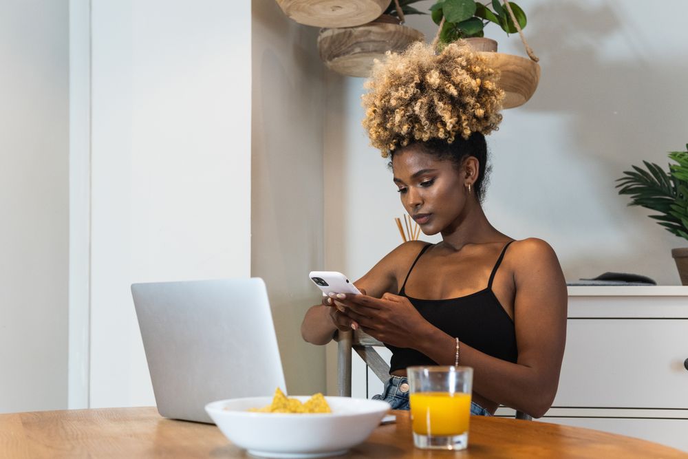Black woman with laptop and mobile phone sitting on chair during breakfast
