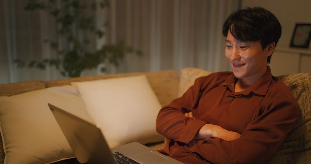 South Korean Man Resting on a Sofa at Home, Using Laptop Computer to Watch Relaxing Videos On the Internet.