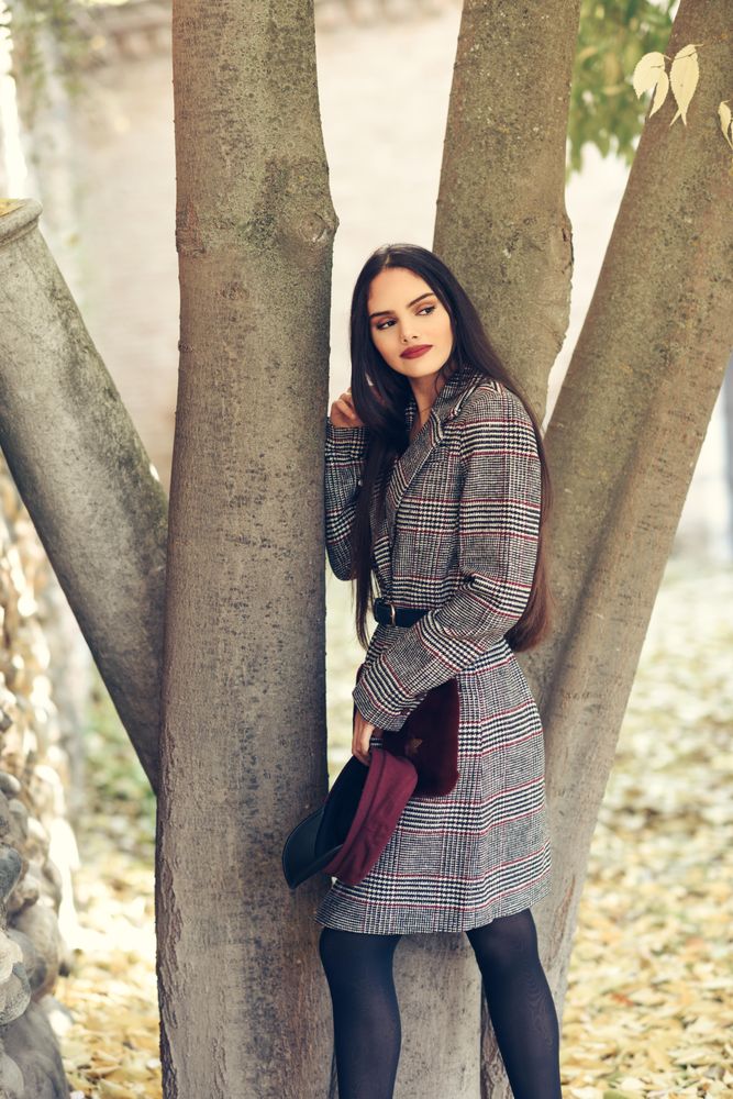 Female looking away in warm winter clothes standing with tree in autumn