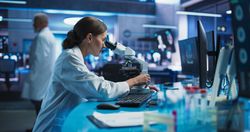 Medical Research And Development Center: Female Scientist Using Microscope To Analyze Petri Dish Sample.