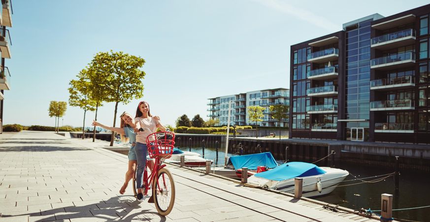 Two close female friends happily walking along the waterfront with red bike