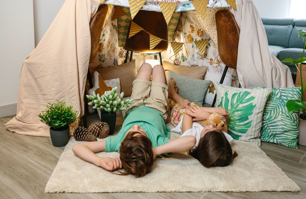 Unrecognizable children relaxing lying over rug in cozy tent at home with playful atmosphere