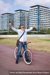Male with colorful bicycle with phone and outstretched arms on city bike path, vertical bG1al5
