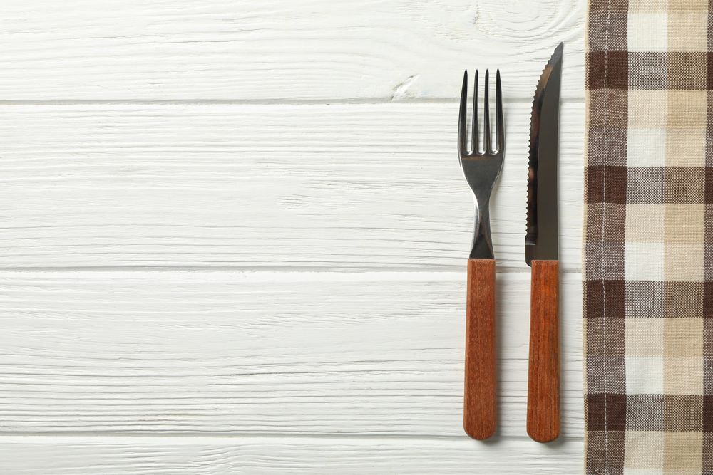 Tablecloth and cutlery on wooden background, space for text