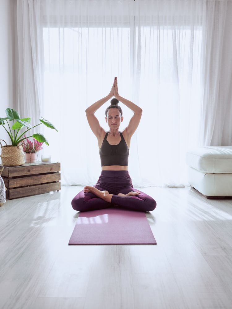 Woman sitting in Padmasana on mat with namaste gesture
