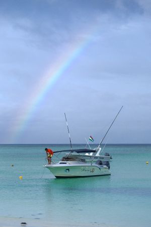 Boat with man on it in Indian Ocean under rainbow