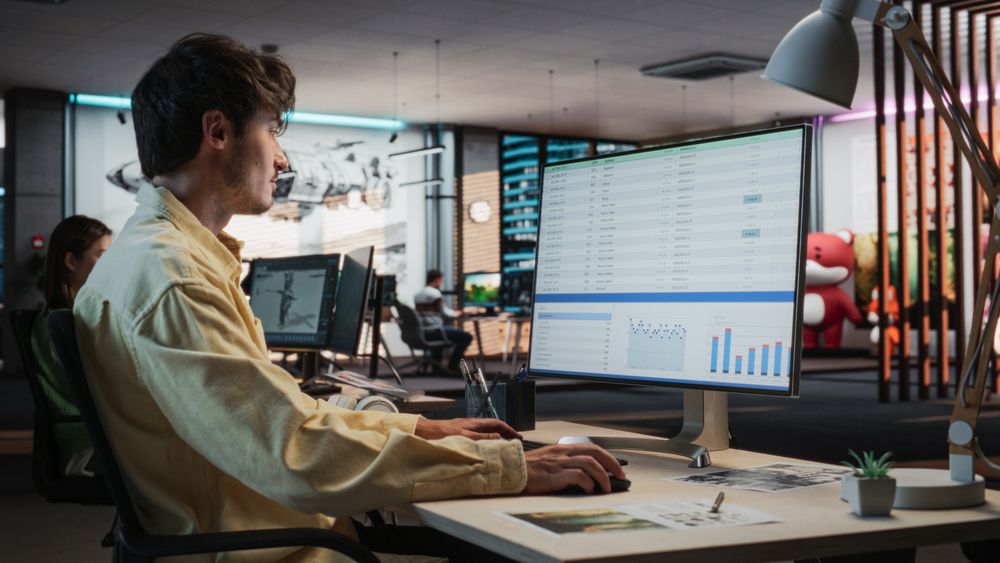 Male Manager Using Desktop Computer With Analytics Software wth Financial Reports.