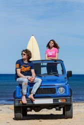 Woman with surfboard and man sitting on car