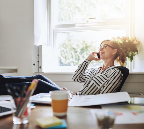 Woman leaning back at her home desk while taking a call