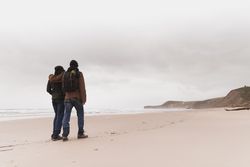 Couple walking on sand shore near water