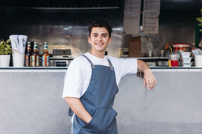 Happy male in apron and leaning on open counter of food truck