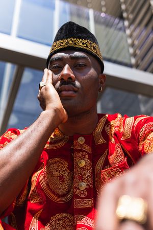Thoughtful Black man in traditional clothes and headdress near building