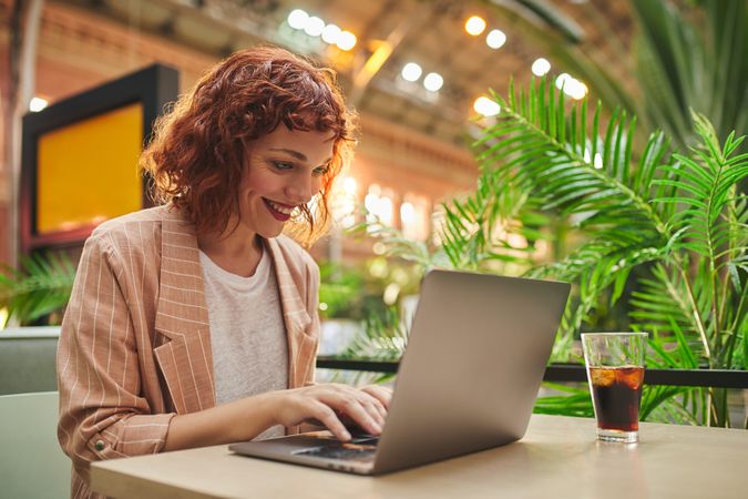Cheerful young woman working on laptop in cafe