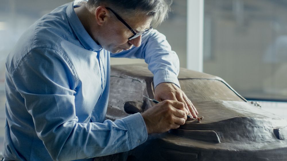Automotive Designer with Rake Sculpts Futuristic  Car Model from Plasticine Clay.