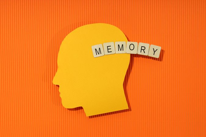 Orange duotone flat lay of head with the word “memory” in wooden blocks