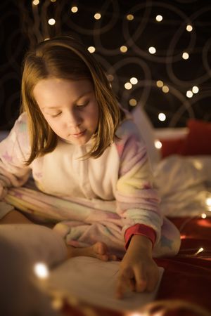 Girl reading book in bedroom decorated with Christmas lights