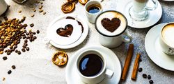 Coffee drinks with foam art on table with cinnamon sticks, dried orange and coffee beans