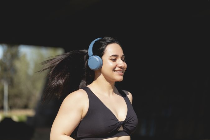 A strong young woman plays sports and runs in the park happy, listening to music with headphones