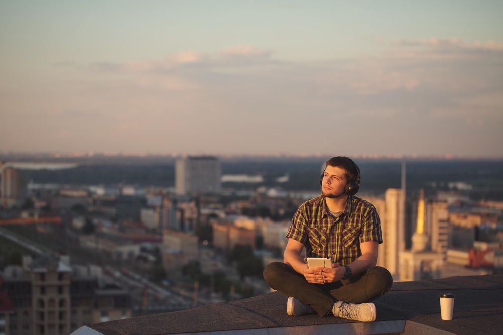 Male using digital tablet with headphones with takeaway coffee cup while enjoying view from roof