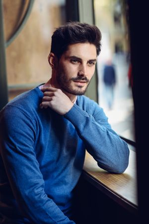 Brown haired male in blue sweater sitting in cafe window