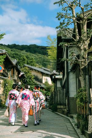 Three women in kimonos walking in pathway
