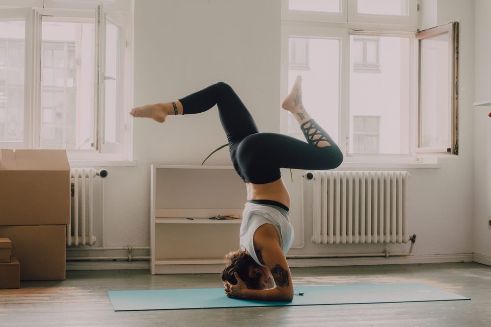 Fit woman practicing yoga pose and standing on head at home
