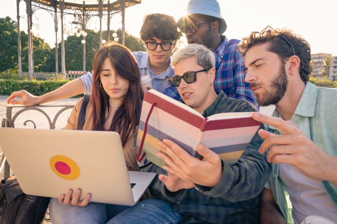 Diverse group of students collaborating with a laptop and tablet on a park bench.
