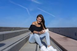 One woman with long hair sitting on staircase while using mobile phone with a big smile
