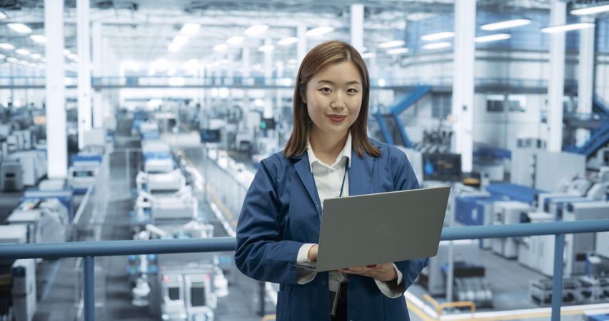 Portrait of an Electronics Manufacture Engineer Smiling, Looking at Camera. Young Japanese Female Using Laptop Computer for Online Research, Monitoring Artificial Intelligence Systems