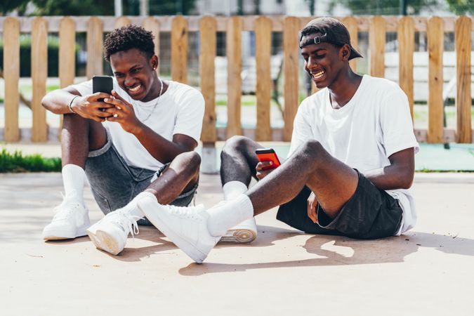 Excited sportive black men looking browsing smartphone while sitting on ground