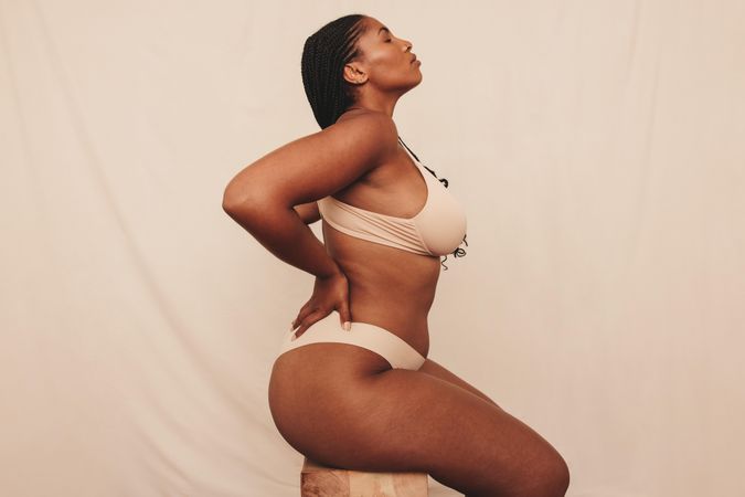 Side view of model with hands on her back wearing tan colored undergarments