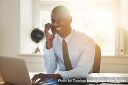 Man in suit and tie smiling on phone while working at his desk 5nLo6b