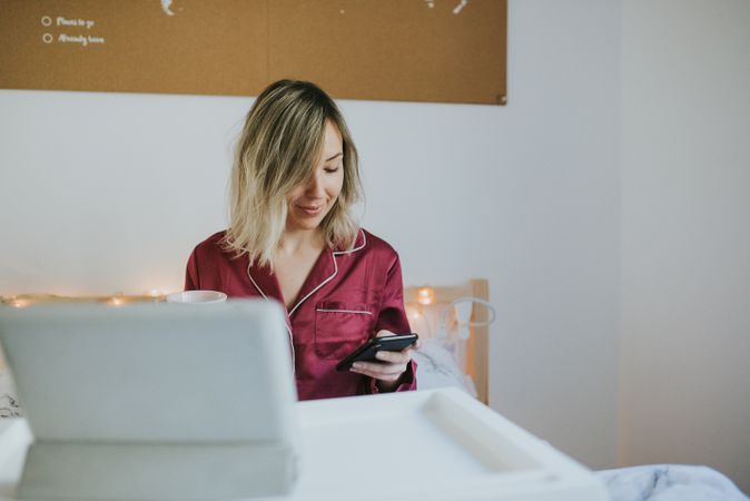 Woman sitting in bed with tablet and looking on smartphone
