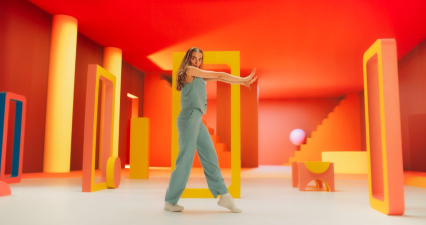 Portrait of White Stylish Female Dancer Performing in a Funky Colorful Decorated Studio While Looking at Camera. Woman Dancing in Abstract Environment, Jumping Through Geometric Shapes