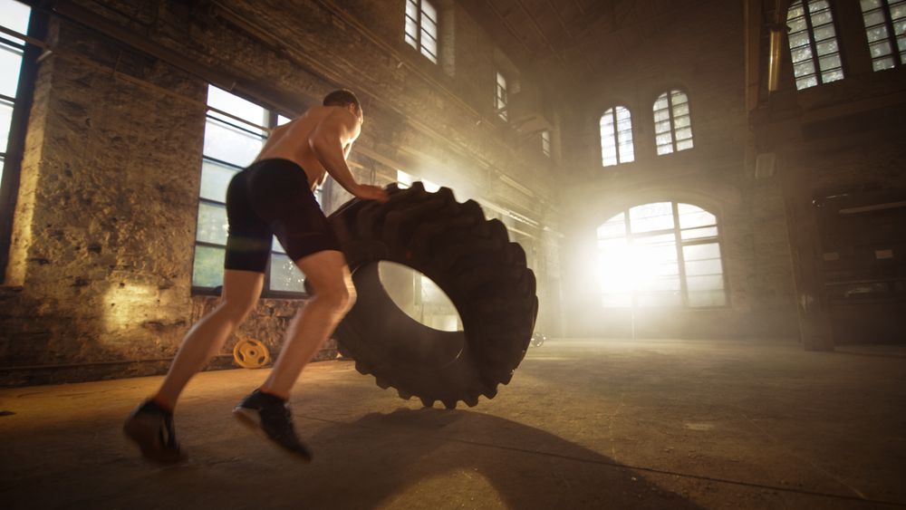 Strong Muscular Man Lifts Tire as Part of His Cross Fitness Program.
