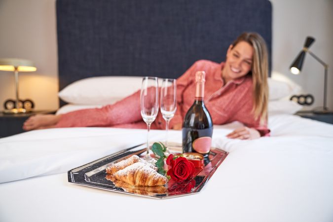 Cheerful woman lying on bed with gifted champagne and rose