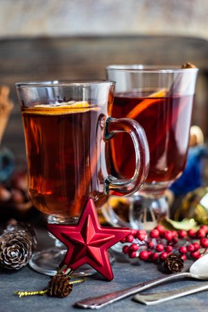 Side view of dried orange slices and cinnamon sticks in mugs of warm drinks