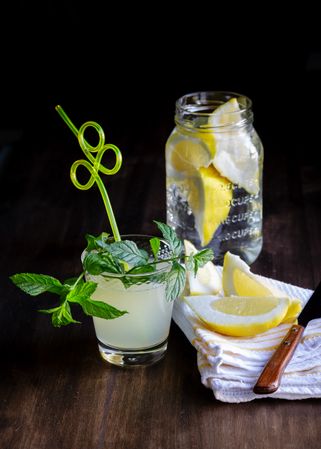 Glass of fresh lemonade next to plate with cut lemons on table