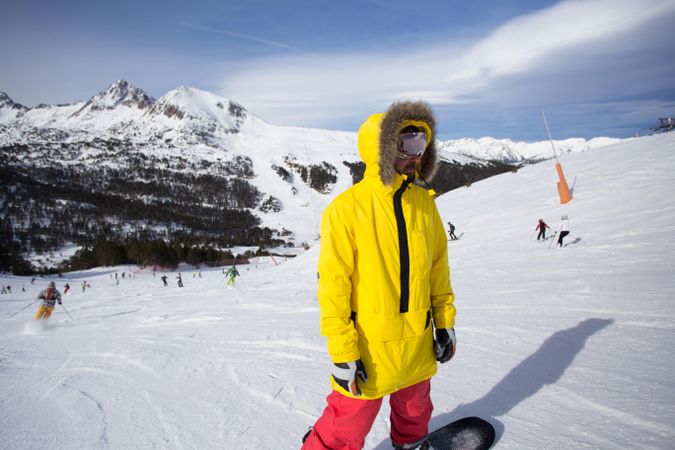 Man in yellow parka on mountain with snowboard