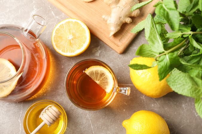 Cup of tea, mint, honey, ginger and teapot on grey background, top view