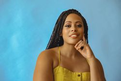Portrait of smiling female with long braided hair with hand on chin in yellow shirt