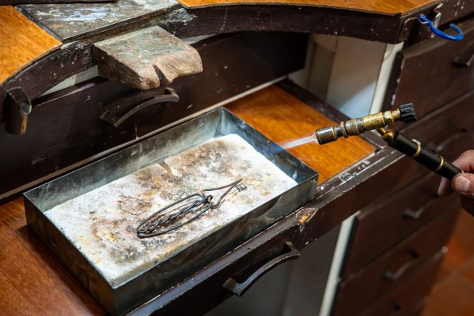 Jeweler melting silver metal with open flame blow torch welding. Goldsmith working and creating in his jewelry workshop.