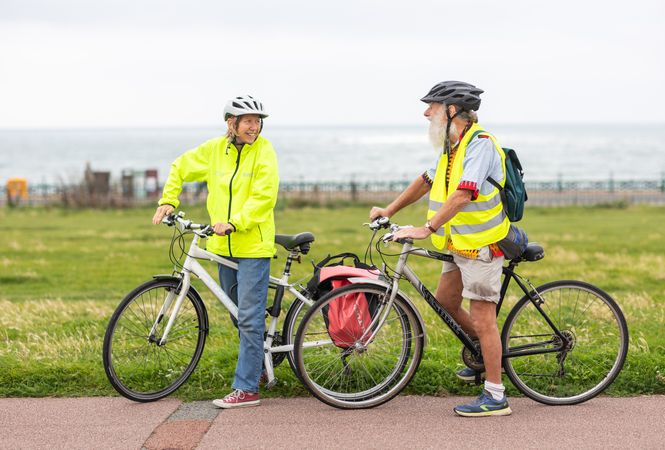 Two older people standing and talking with bikes looking away by the waterfront
