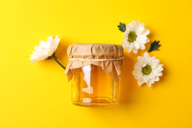 Glass jar with honey and chamomile on yellow background, space for text