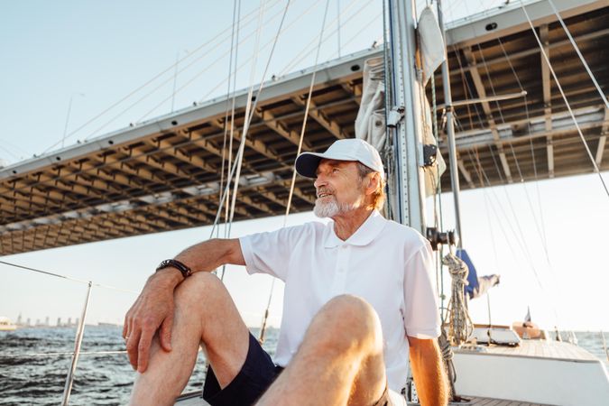 Mature captain relaxing on sailboat as it goes under a bridge